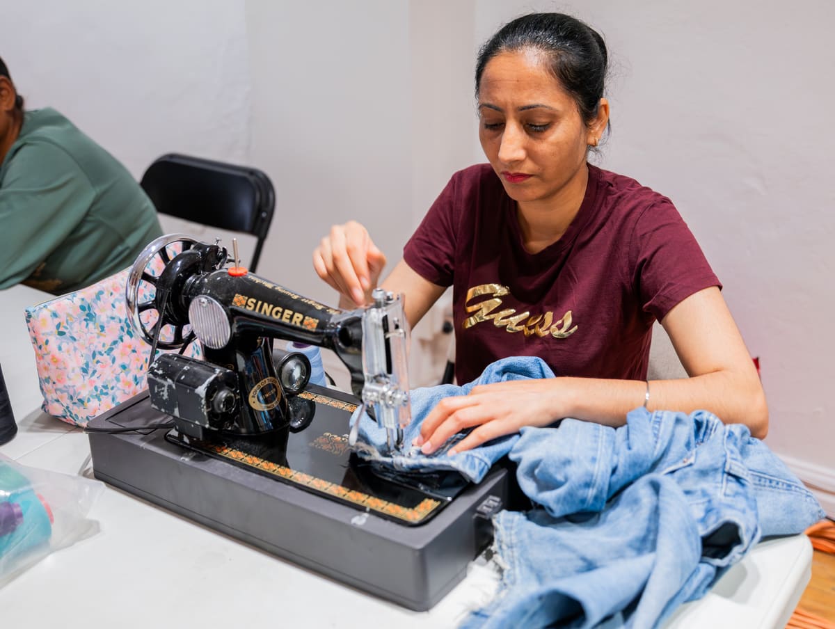 Une membre de l’atelier retouche un vêtement en denim à la machine à coudre.